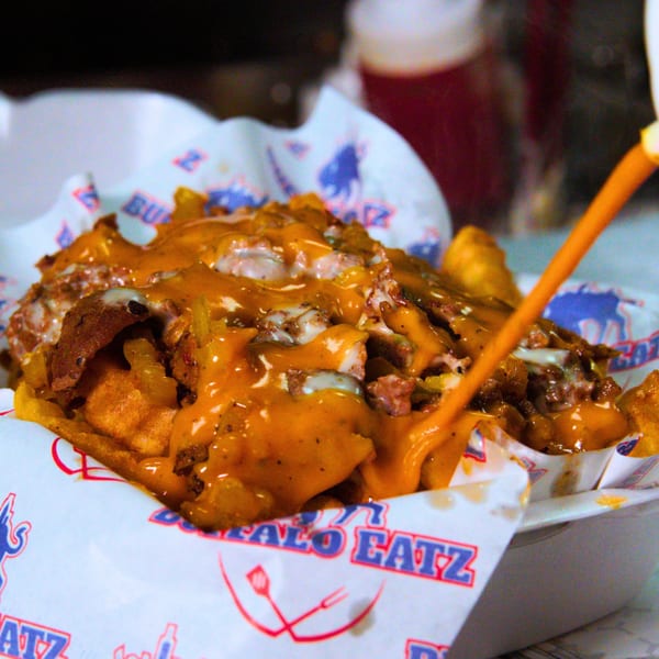 Buffalo Eatz loaded fries with melted cheese, meat, and sauce being drizzled on top.