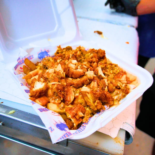 Buffalo Eatz's loaded fries with crispy chicken pieces and a savory sauce in a takeout container.