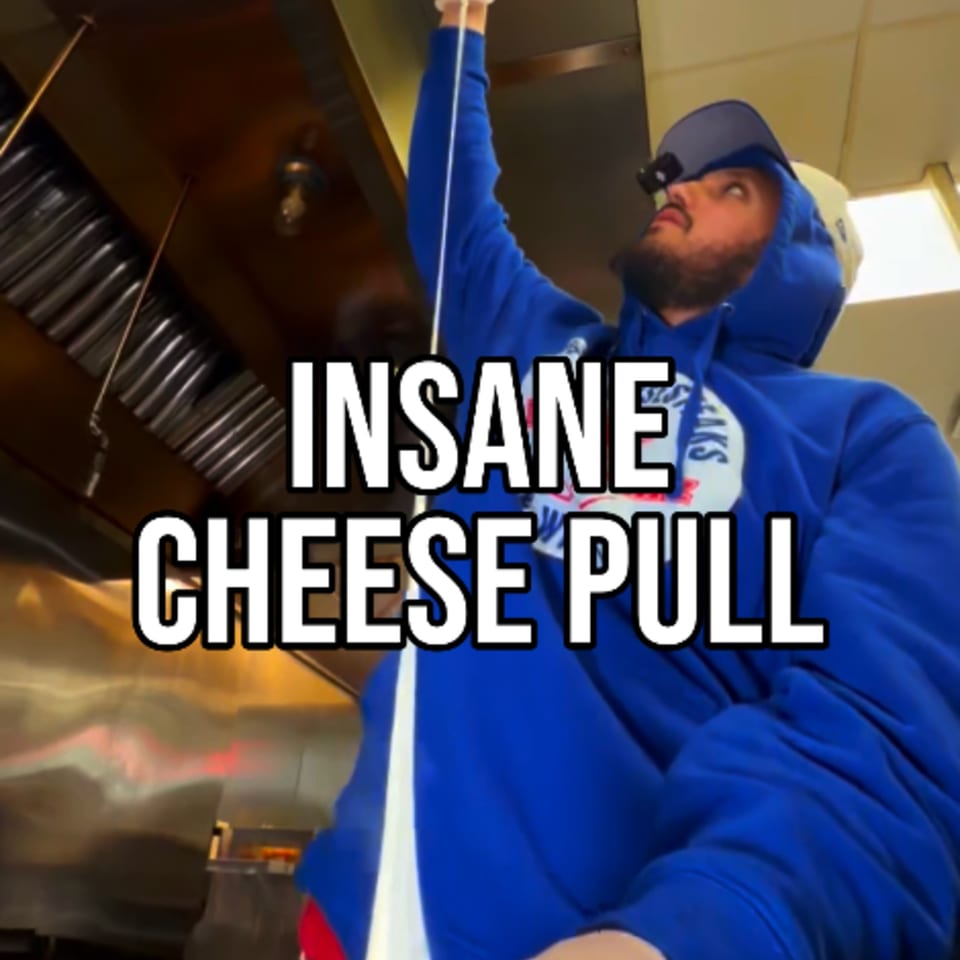 Man in blue hoodie pulling a long string of melted cheese from a Buffalo Eatz dish.