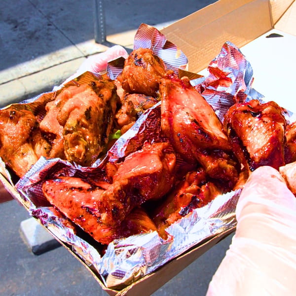 A box of Buffalo Eatz chicken wings, some with red sauce, held by gloved hands.